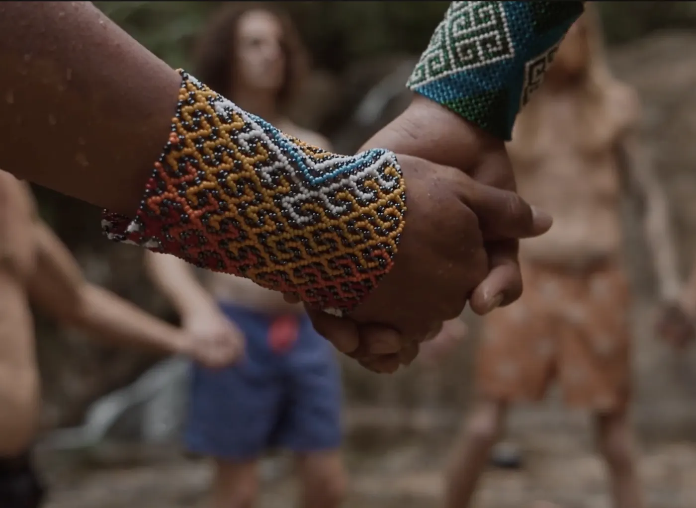 Two hands holding each other, beaded bracelets on the wrists, with guests behind